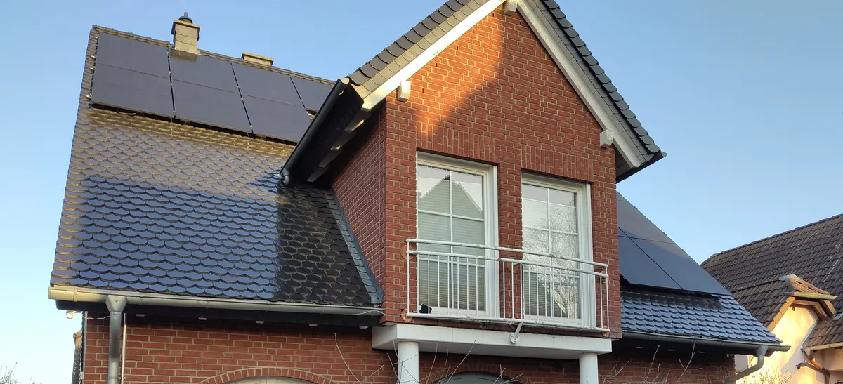 Brick house with a dark slate roof carrying rows of all-black solar modules that blend into the roof surface