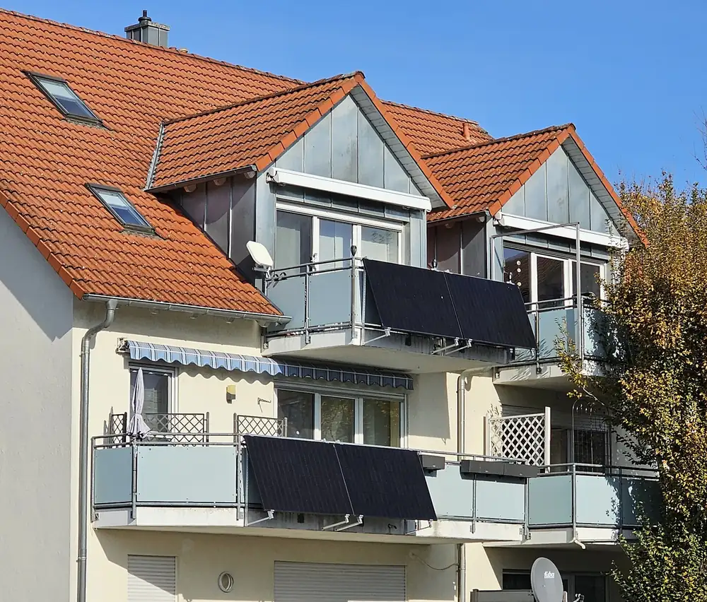 Two balconies of a house each carrying a pair of black solar modules tilted outward on railing brackets