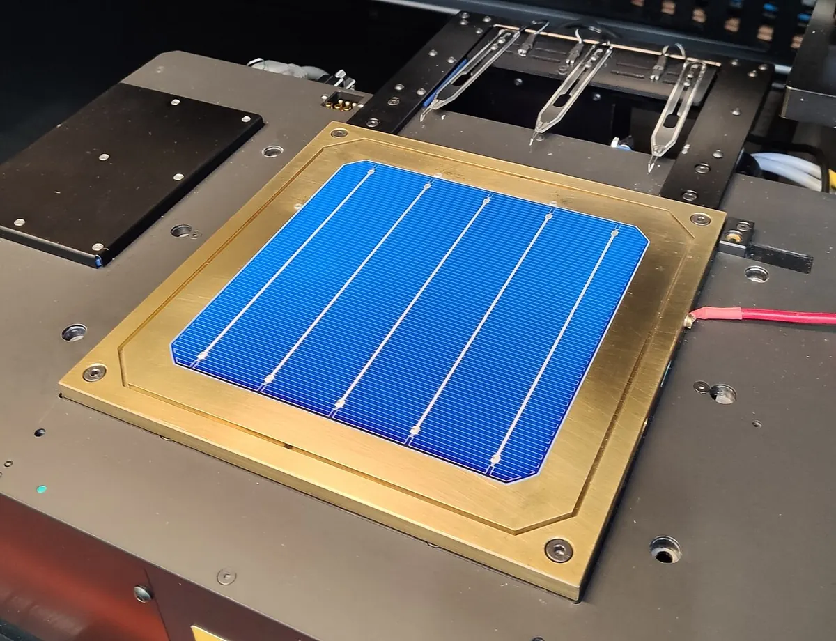 Blue silicon heterojunction solar cell with busbars lying on a gold-coloured measurement stage in a laboratory