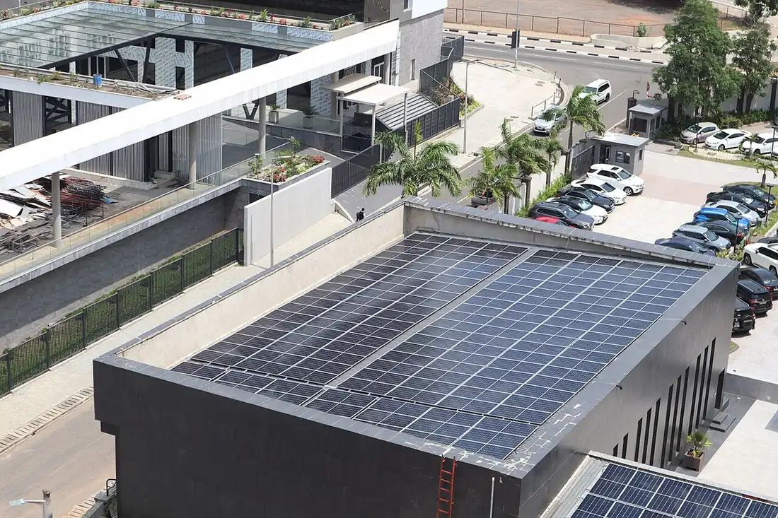 Rows of solar modules covering a flat commercial building roof, seen from above beside a car park