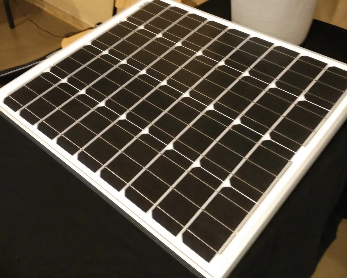 Small monocrystalline solar module on a table, dark pseudo-square cells separated by white gaps inside a silver aluminium frame