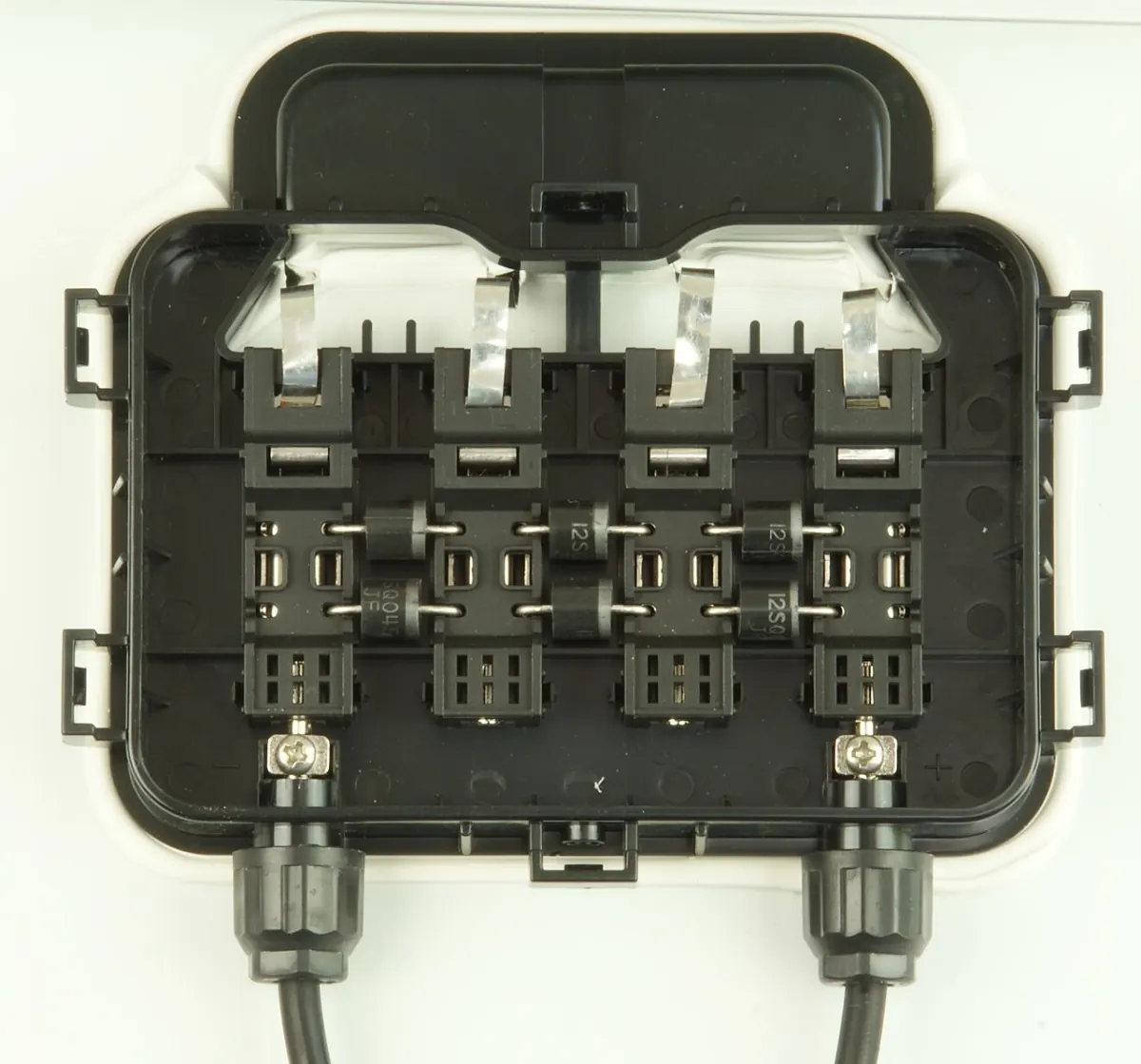 Opened solar module junction box showing bypass diodes, ribbon contacts and two output cables