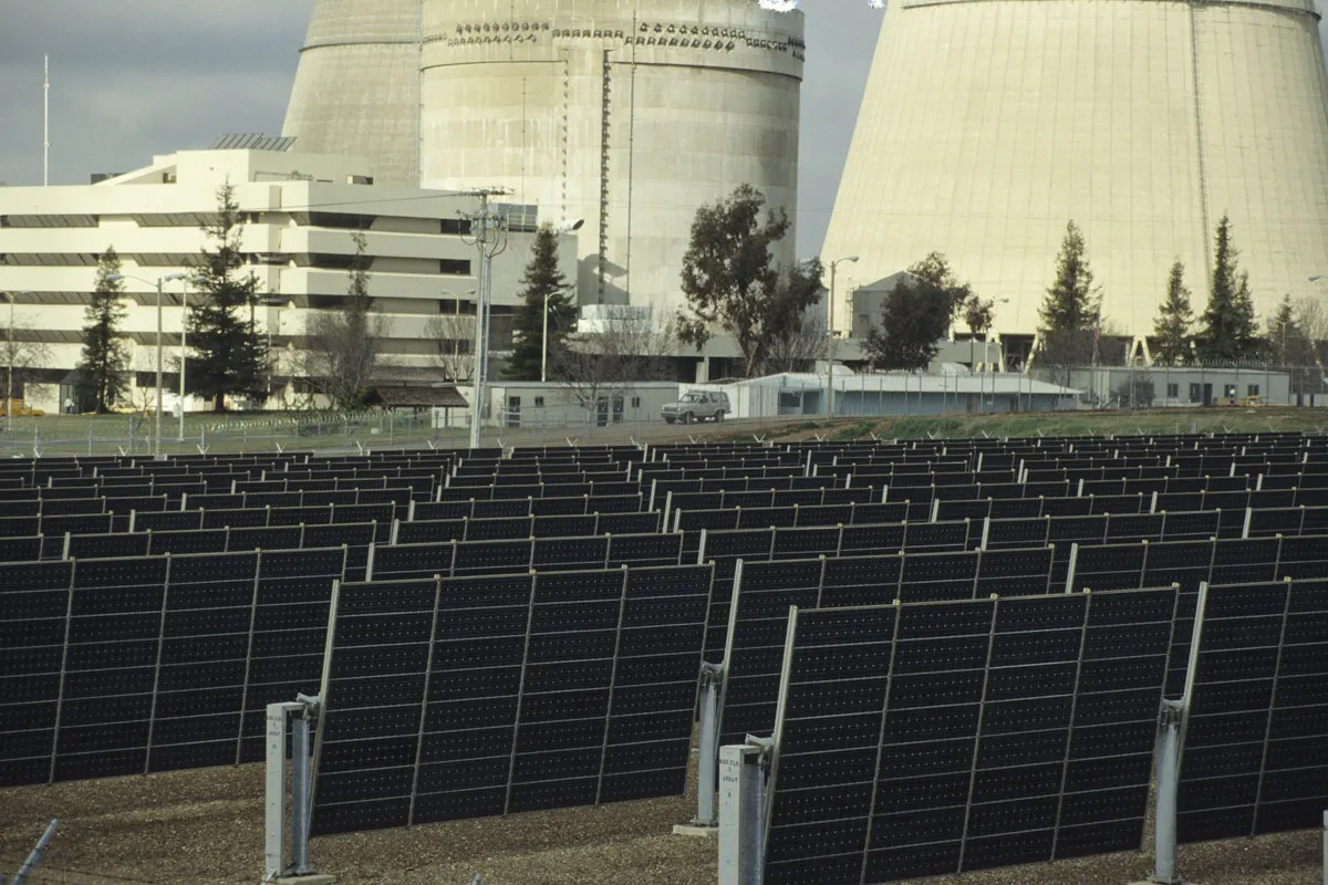 Rows of dark solar modules on single-axis trackers in front of the cooling towers of the Rancho Seco power plant in California