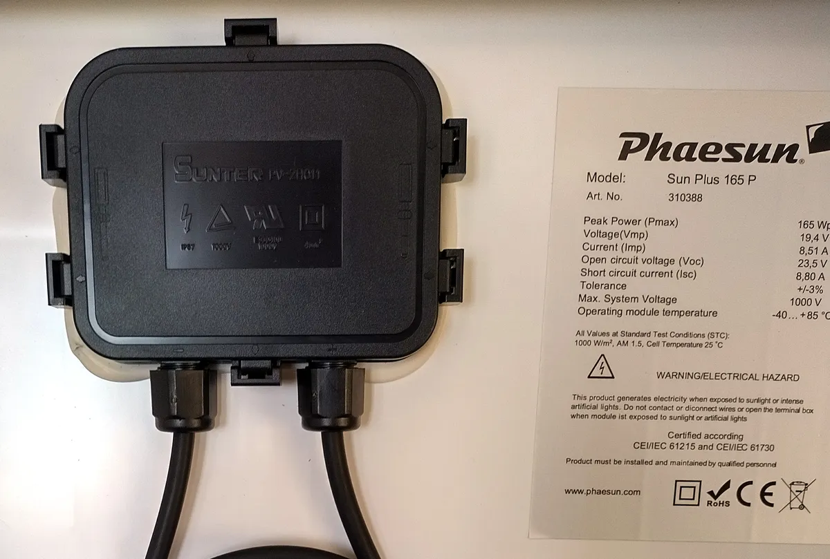 Back of a small solar module with a black junction box beside a white rating label that reads Certified according CEI/IEC 61215 and CEI/IEC 61730, above a row of marks including CE