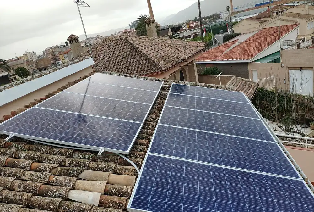 Two groups of blue solar modules on a clay tile roof with neighbouring rooftops behind